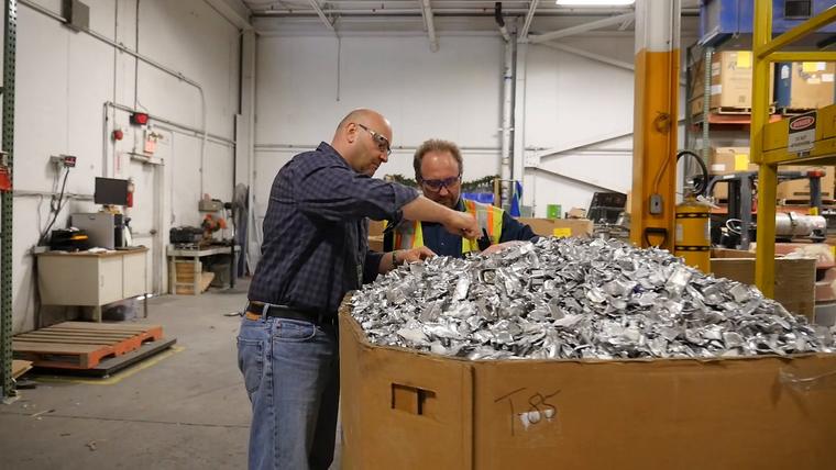 Two people checking a large box of shredded metal on the plant floor